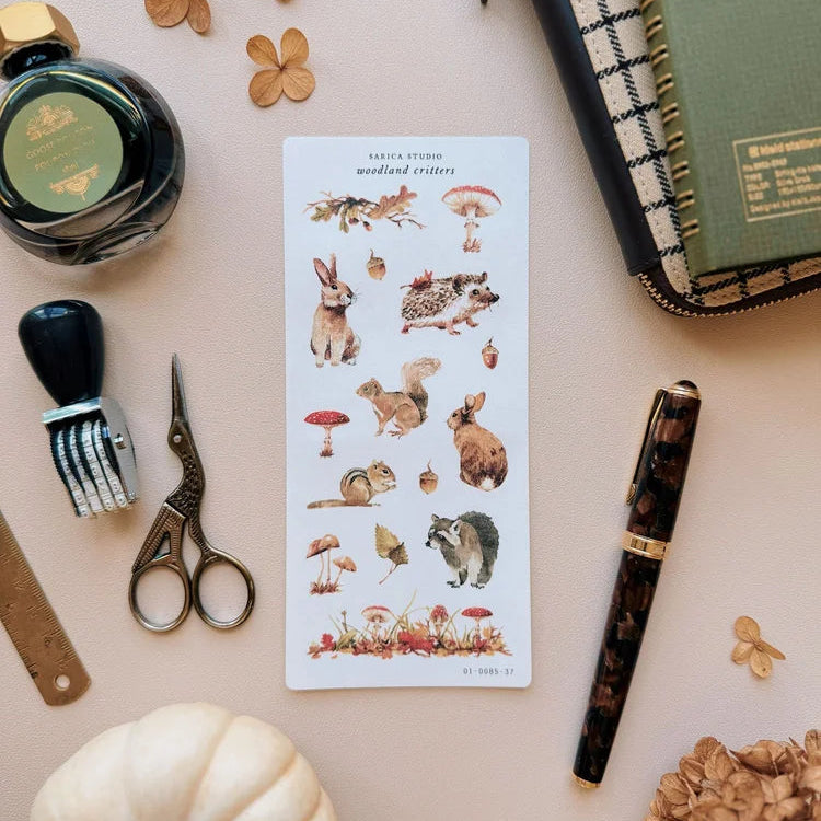Sheet of nature-themed stickers with animals and plants on a desk with stationery items.